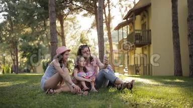 妈妈和两个女儿坐在棕榈树附近的草地上。 日落时公园里的孩子和母亲。 投<strong>标</strong>书